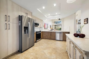 Eine moderne Küche mit Edelstahl-Kühlschrank, Backofen und Geschirrspüler, Holzschränken und einer Marmorarbeitsplatte.