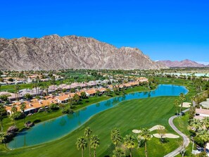 Ein Golfplatz mit Wasserspiel, umgeben von Wohngebäuden und Bergen.