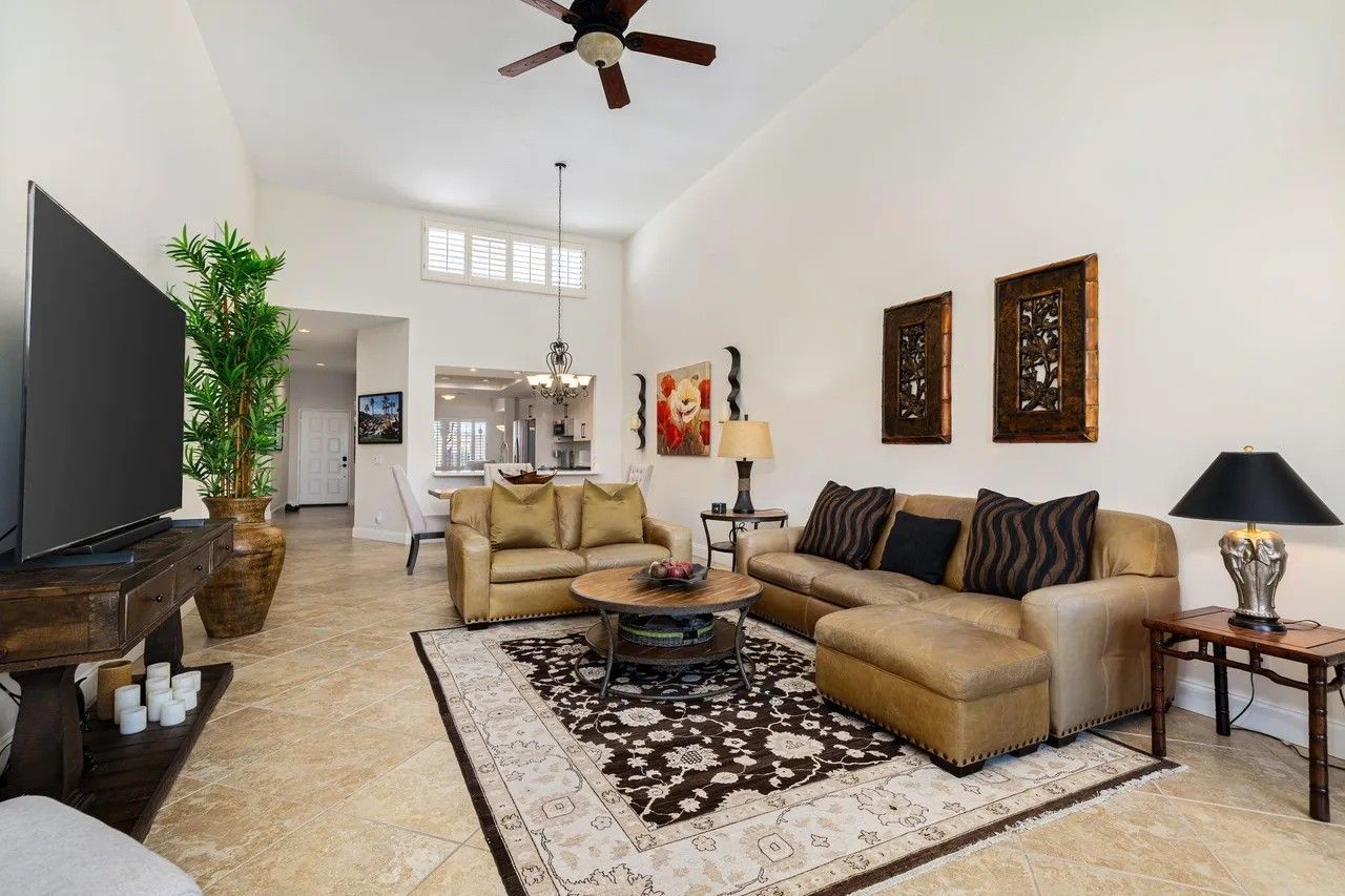 A spacious living room with a large flat-screen TV, two sofas, a coffee table, and a ceiling fan.