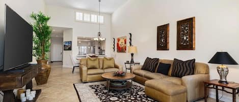A spacious living room with a large flat-screen TV, two sofas, a coffee table, and a ceiling fan.