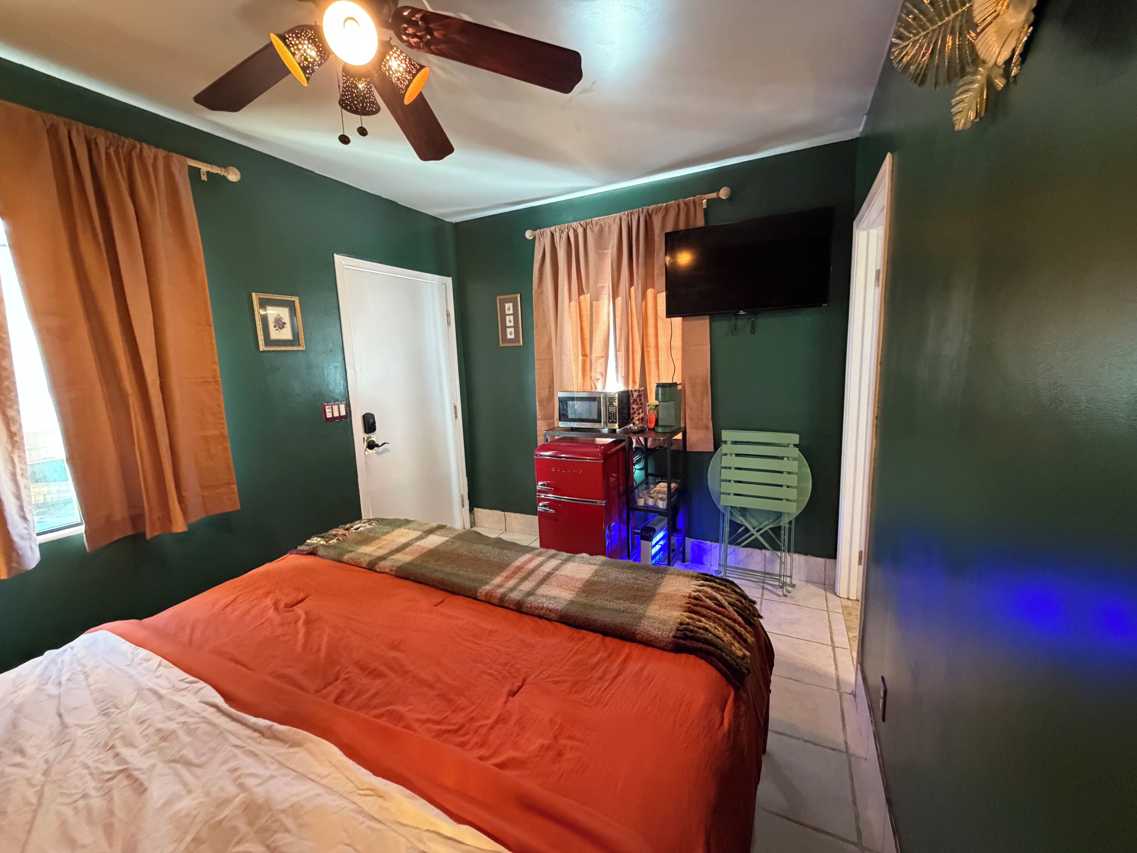 Une chambre à coucher avec un lit, un ventilateur de plafond, une télévision et une commode.