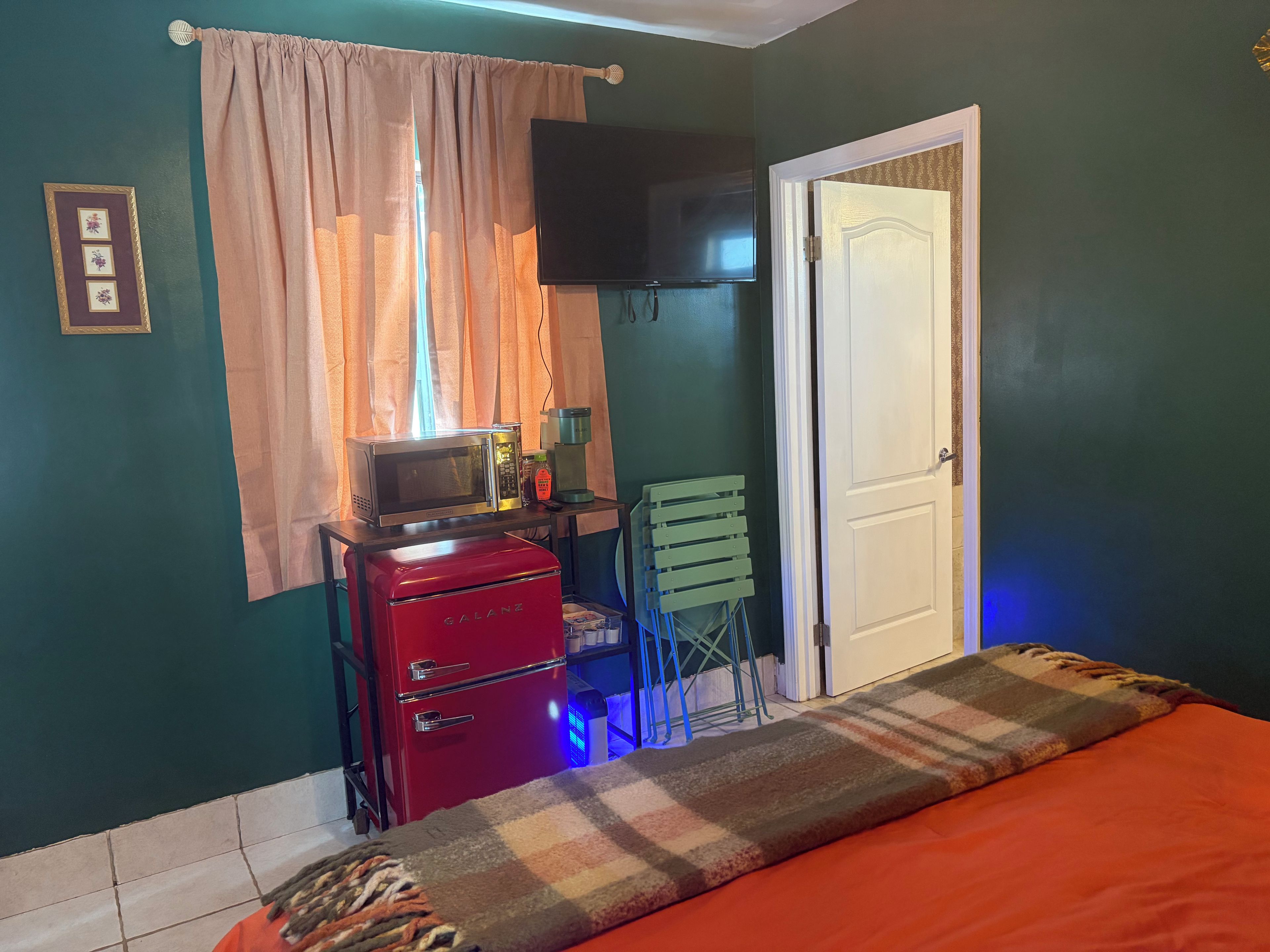Une pièce avec un lit, un appareil électroménager rouge, un téléviseur et une porte.
