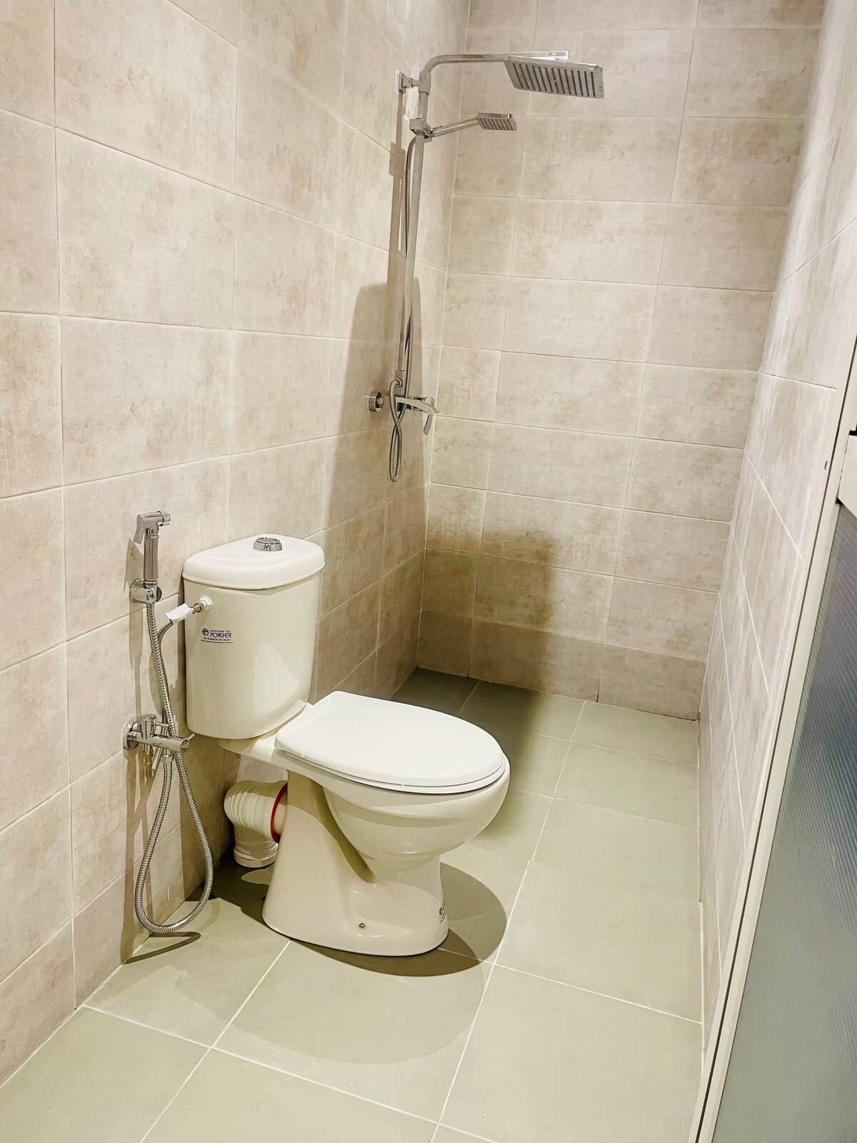 Un baño con inodoro, ducha y suelo de baldosas.