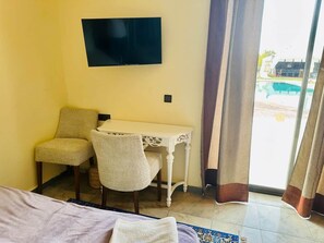 Une chambre d’hôtel équipée d’un lit, d’un bureau, de deux chaises, d’une télévision et offrant une vue sur une piscine.