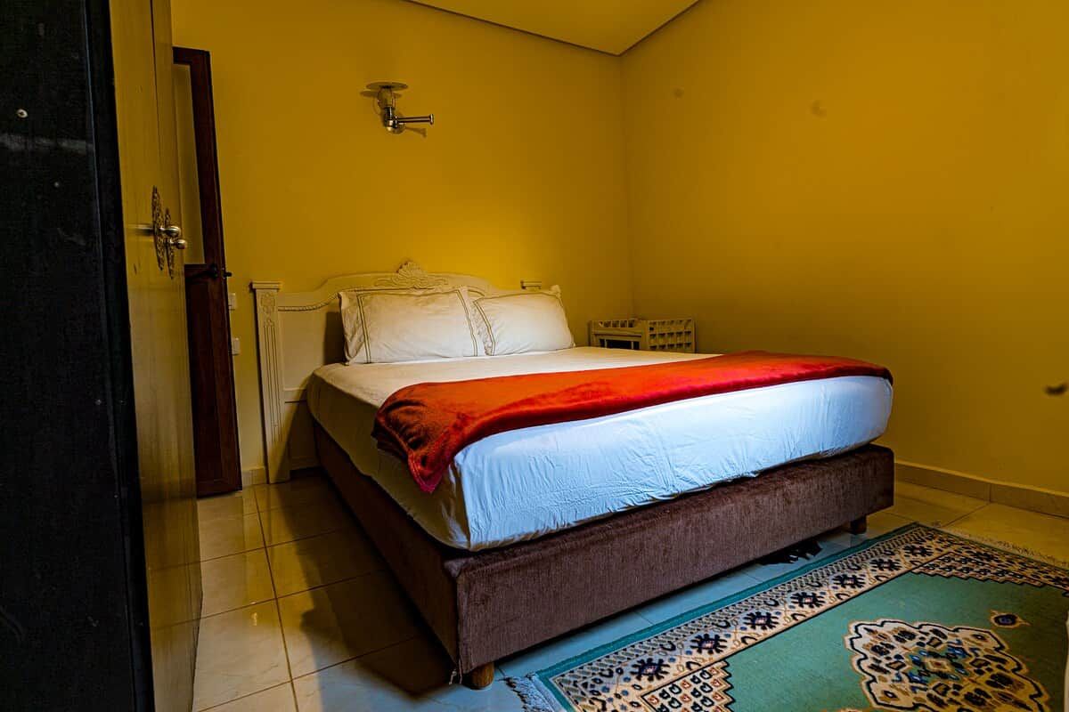 Una habitación con cama, una puerta y una lámpara fijada a la pared.