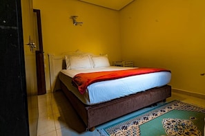 Una habitación con cama, una puerta y una lámpara fijada a la pared.