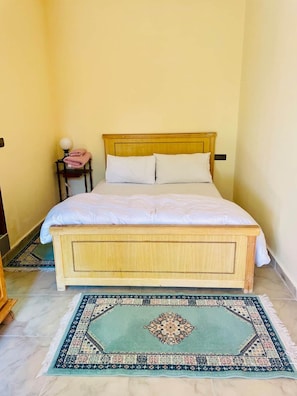 Una cama individual con cabecera de madera y ropa de cama blanca en una habitación con paredes amarillas.