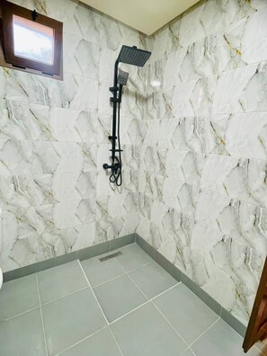 Un baño con ducha, paredes de mármol y una ventana.