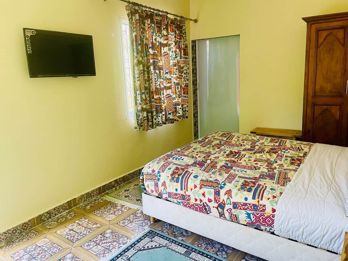 Un dormitorio con cama, televisor en la pared, cortina estampada y armario de madera.