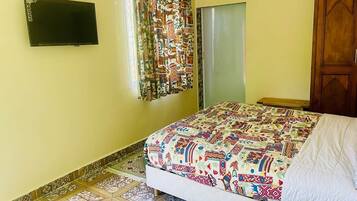Un dormitorio con cama, televisor en la pared, cortina estampada y armario de madera.