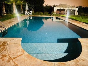 A swimming pool with a tiled deck, a covered seating area, and a gazebo in the background. - Triple Room + Pool Access (Tassoultante)