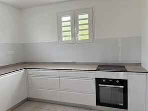 A kitchen with white cabinets, a black oven, and a window with a view of greenery. - New Listing (Sainte-Luce)