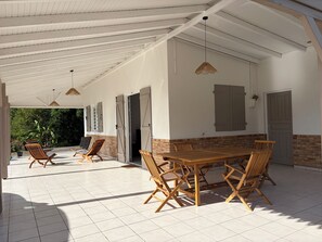 An outdoor covered patio with a wooden table and chairs, a ceiling with exposed beams, and a view of greenery outside. - New Listing (Sainte-Luce)