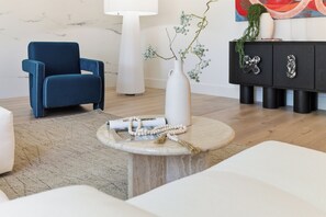 A modern living room with a blue chair, a white vase with branches, a round table with a magazine, and a black cabinet with decorative items. - Newer 4BR Luxury Home in West San Jose — 2 Primary Suites, Minutes to Apple Park (San Jose)