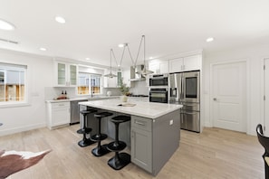 A modern kitchen with a central island, bar stools, stainless steel appliances, and a large window. - Newer 4BR Luxury Home in West San Jose — 2 Primary Suites, Minutes to Apple Park (San Jose)