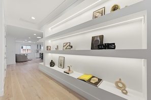 Interior moderno com paredes brancas e soalho de madeira, apresentando um longo corredor com estantes embutidas exibindo diversos objetos.