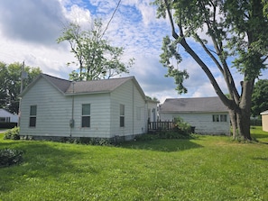 A two-story white house with a sloped roof, surrounded by a grassy yard and a large tree. - Carico Comfortable Family Home Near Champaign (Tuscola)