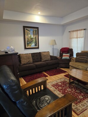 A living room with a dark brown sofa, a black leather chair, a wooden coffee table, and a red patterned rug. - Carico Comfortable Family Home Near Champaign (Tuscola)