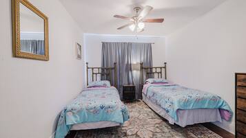A bedroom with two single beds, a ceiling fan, a large mirror, and a patterned rug.