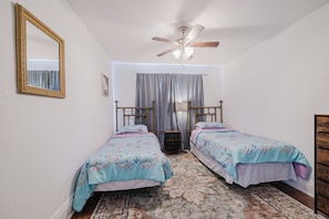 Une chambre avec deux lits simples, un ventilateur de plafond, un grand miroir et un tapis à motifs.