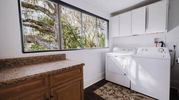 A laundry room with a washing machine, dryer, cabinets, and a large window with a view of trees.