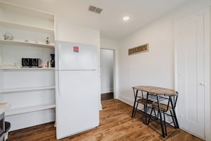 Une petite cuisine avec un réfrigérateur blanc, une petite table avec deux chaises et une enseigne « BAKERY » accrochée au mur.