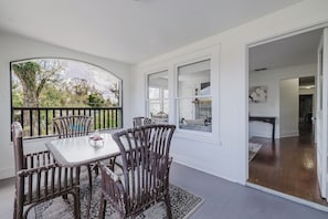 Un espace repas comprenant une table et des chaises, avec vue sur l’extérieur, et une porte-fenêtre donnant sur une autre pièce.