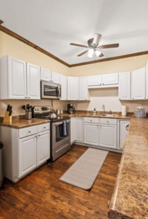 A kitchen with white cabinets, a granite countertop, a ceiling fan, and a wooden floor. - The Flat on Fifth (Knoxville)