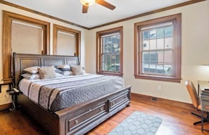 A bedroom with a large bed, wooden headboard, two windows, and a ceiling fan. - The Flat on Fifth (Knoxville)