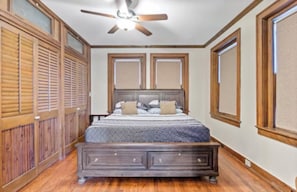 A bedroom with a wooden bed, a ceiling fan, and a large window. - The Flat on Fifth (Knoxville)