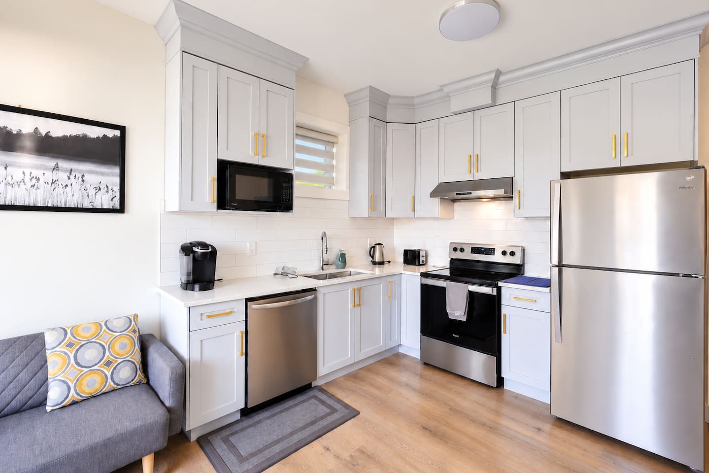 A modern kitchen with white cabinets, stainless steel appliances, and a gray sofa with patterned cushions.