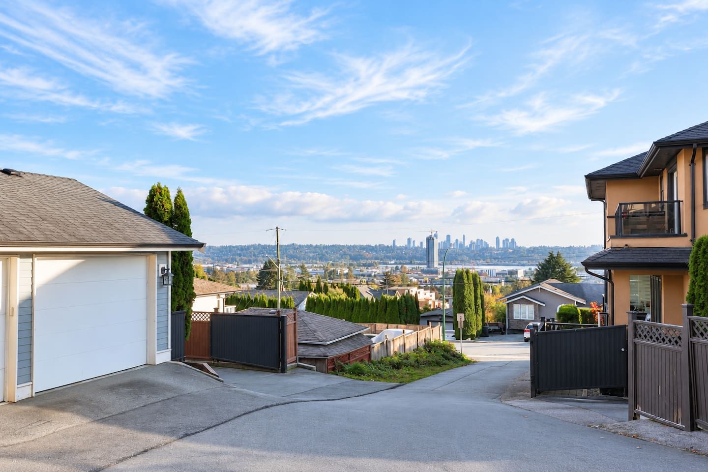 A residential street with houses, a clear sky, and a distant city skyline.