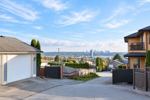 Una calle residencial con casas, cielo despejado y un horizonte urbano lejano.