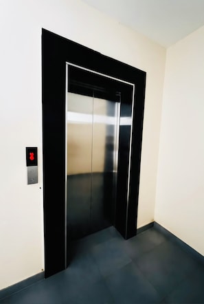 A modern elevator with a metallic finish and a black frame, located in a hallway with light-colored walls and dark flooring. - Modern 1-bedroom apartment in Roysambu, Nairobi, near TRM Mall. (Nairobi)