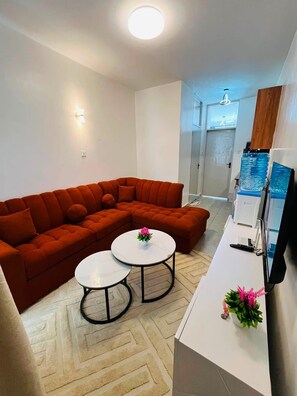 A modern living room with a sectional sofa, two round coffee tables, and a flat-screen TV on a white cabinet. - Modern 1-bedroom apartment in Roysambu, Nairobi, near TRM Mall. (Nairobi)