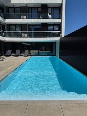 A modern building with a swimming pool, outdoor seating, and a covered area with umbrellas. - Espectacular loft en Buceo con amenities de lujo (Montevideo)