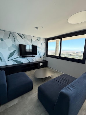 A modern living room with a flat-screen TV, two blue sofas, a small coffee table, and a large window offering a city view. - Espectacular loft en Buceo con amenities de lujo (Montevideo)