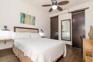 A hotel room with a bed, bedside table, lamp, ceiling fan, artwork, and a mirror. - Cozy 2BR Condo in Downtown Playa del Carmen Prime Location (Playa del Carmen)