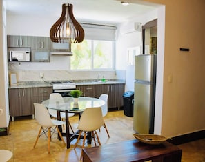 A modern kitchen with a dining table, chairs, and a hanging light fixture. - Cozy 2BR Condo in Downtown Playa del Carmen Prime Location (Playa del Carmen)