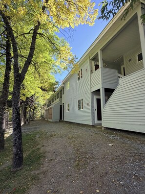 A row of single-story buildings with a gravel driveway and trees with yellow leaves.