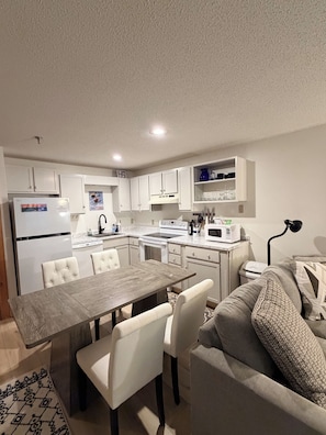 A modern kitchen with white cabinetry, a dining table with chairs, and a sofa in the living area.