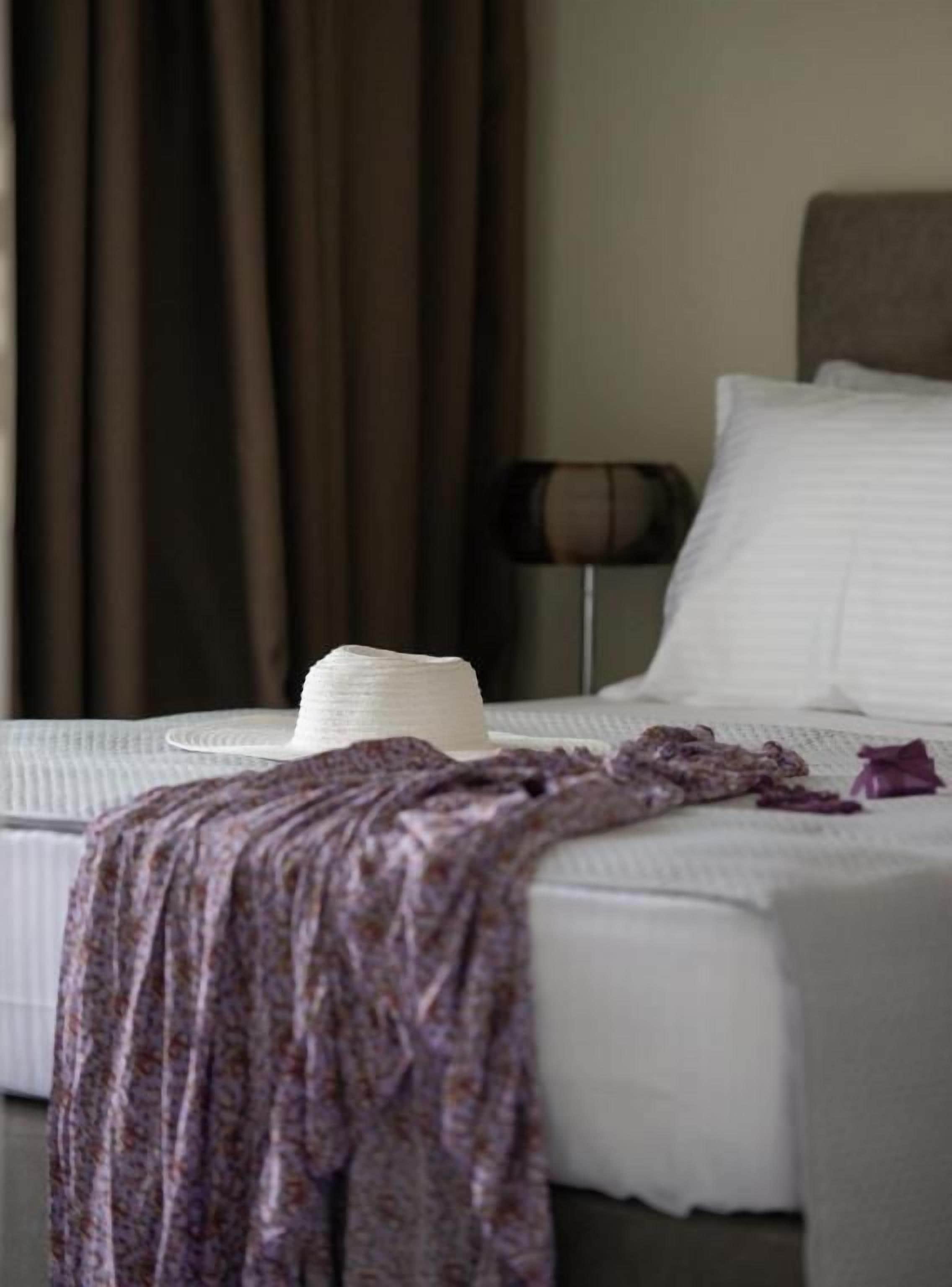 A bed with a white comforter and a decorative hat on it.