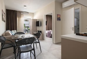 A modern hotel room with a dining area, a TV mounted on the wall, and a separate bathroom. - Crist Luxury Apartments (Nea Potidea)