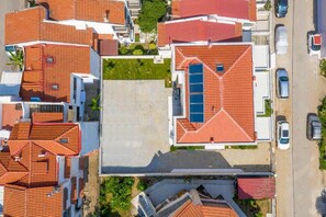 An aerial view of a residential area with multiple houses, each with red-tiled roofs, and a central open space with a blue swimming pool. - Crist Luxury Apartments (Nea Potidea)