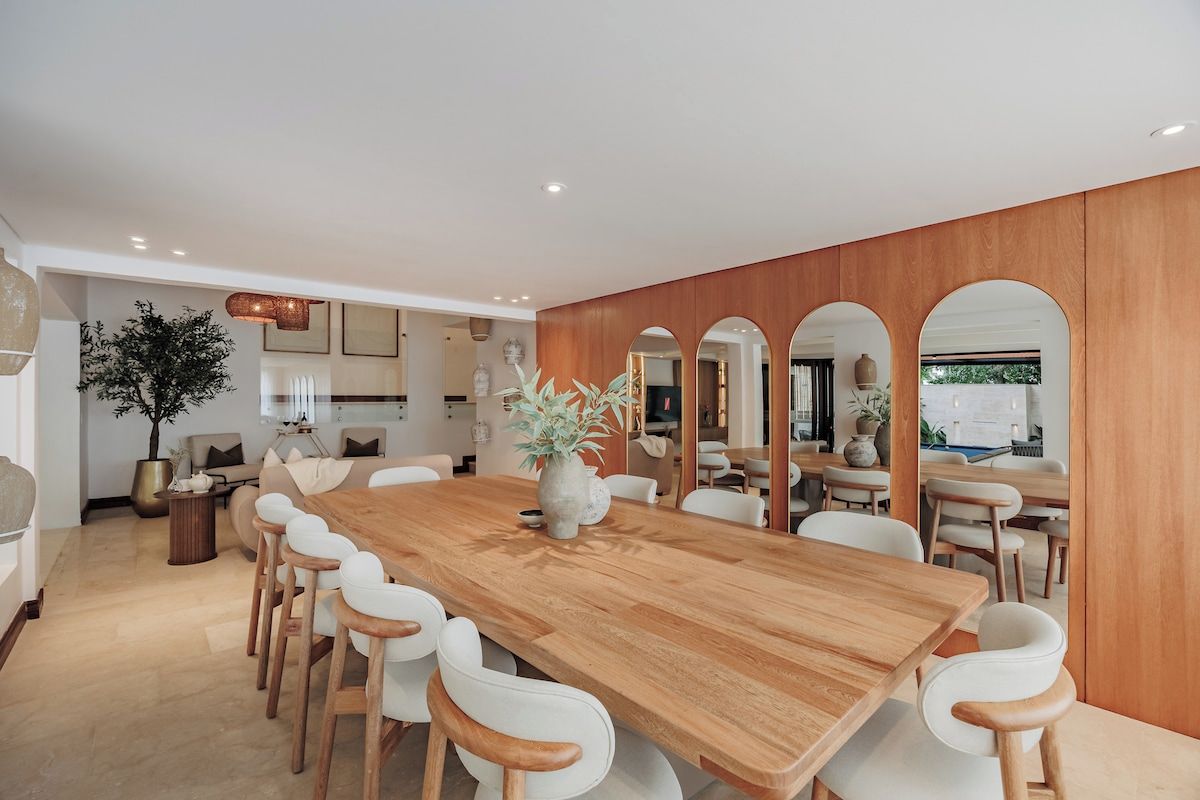 Un'ampia sala da pranzo con un lungo tavolo in legno e sedie bianche, circondata da pannelli di legno e finestre ad arco.