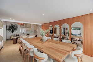 A spacious dining area with a long wooden table and white chairs, surrounded by wooden paneling and arched windows. - Villa Bonita Estate · Private Retreat · El Poblado (Medellín)