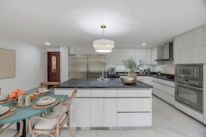 Una cocina moderna con una isla central, electrodomésticos de acero inoxidable y una zona de comedor con una mesa dispuesta para cuatro.