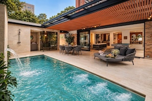 A swimming pool with a waterfall feature, surrounded by outdoor seating and a covered patio area. - Villa Bonita Estate · Private Retreat · El Poblado (Medellín)