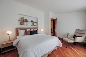 A bedroom with a bed, bedside tables, a chair, and a shelf with decorative items. - Villa Bonita Estate · Private Retreat · El Poblado (Medellín)
