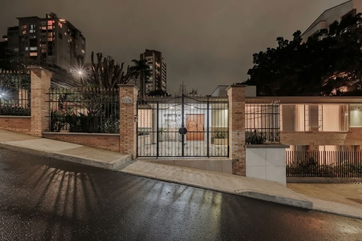 A gated entrance with a metal gate and a brick wall, leading to a building with a modern design.